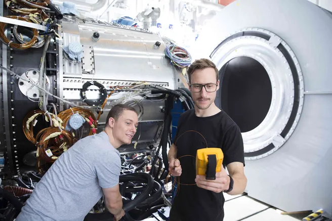 Two students hold a device in their hands and stand next to a large machine.